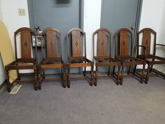 Row of five wooden dining chairs with dark cushions against a wall on a carpeted floor