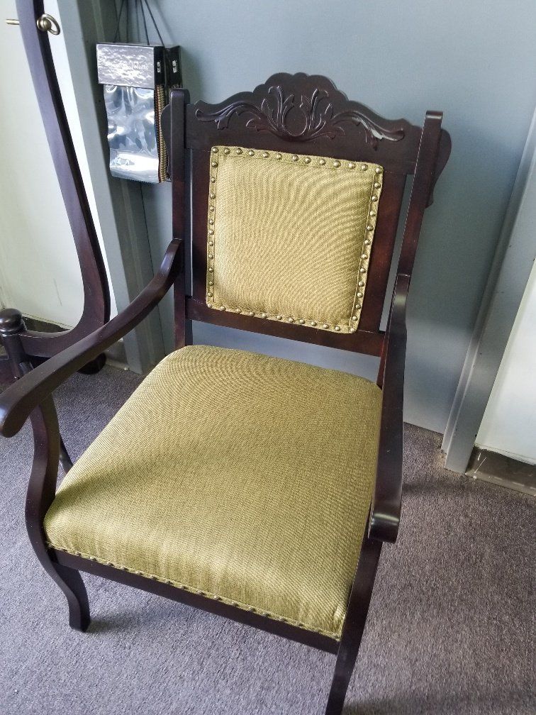 Antique wooden armchair with yellow upholstered seat and back against a gray wall.