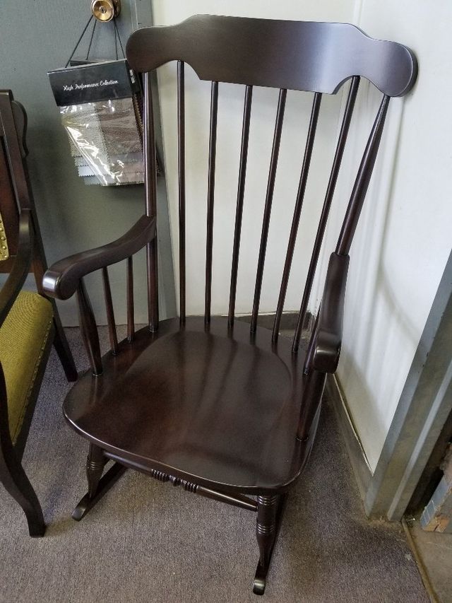 Dark wooden rocking chair with spindle back in a corner next to a wall-mounted bag.