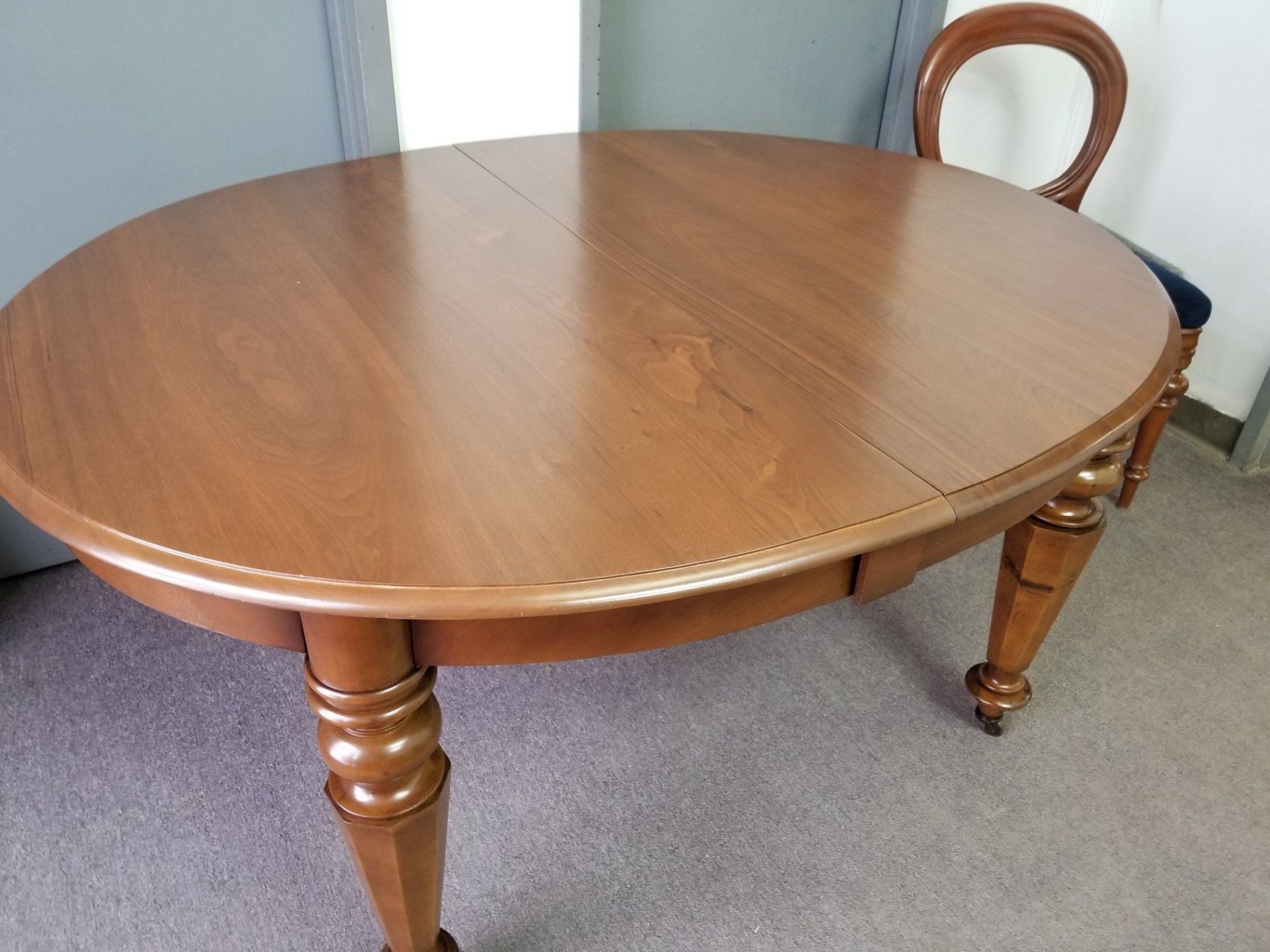 Oval wooden dining table with turned legs in a carpeted room