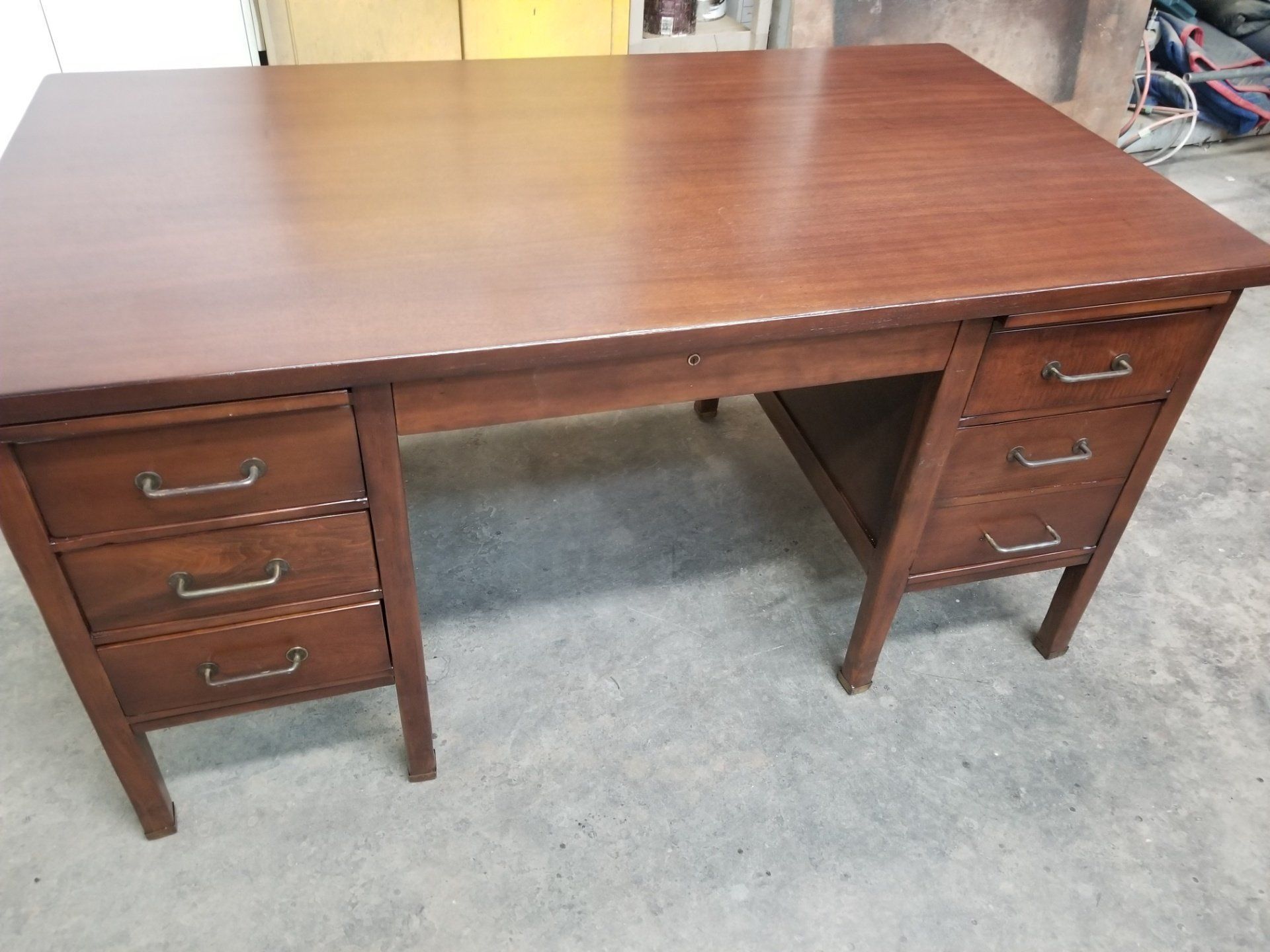 Brown wooden desk with drawers on both sides, shown on a carpeted floor.