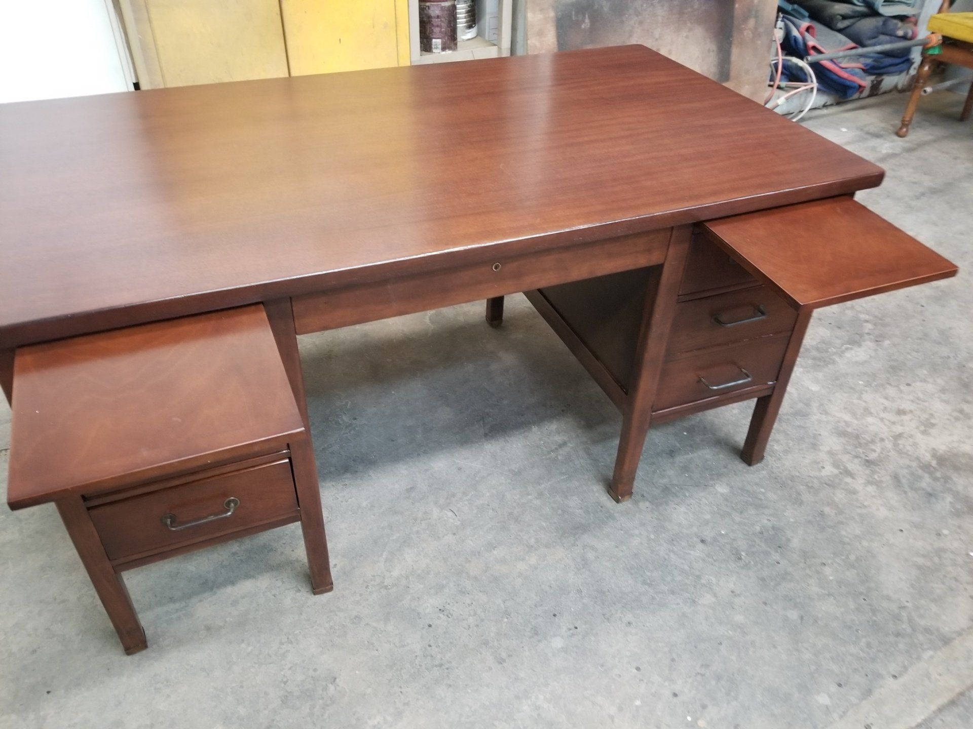 Wooden executive desk with two side pedestals and a pull-out writing shelf on a concrete floor