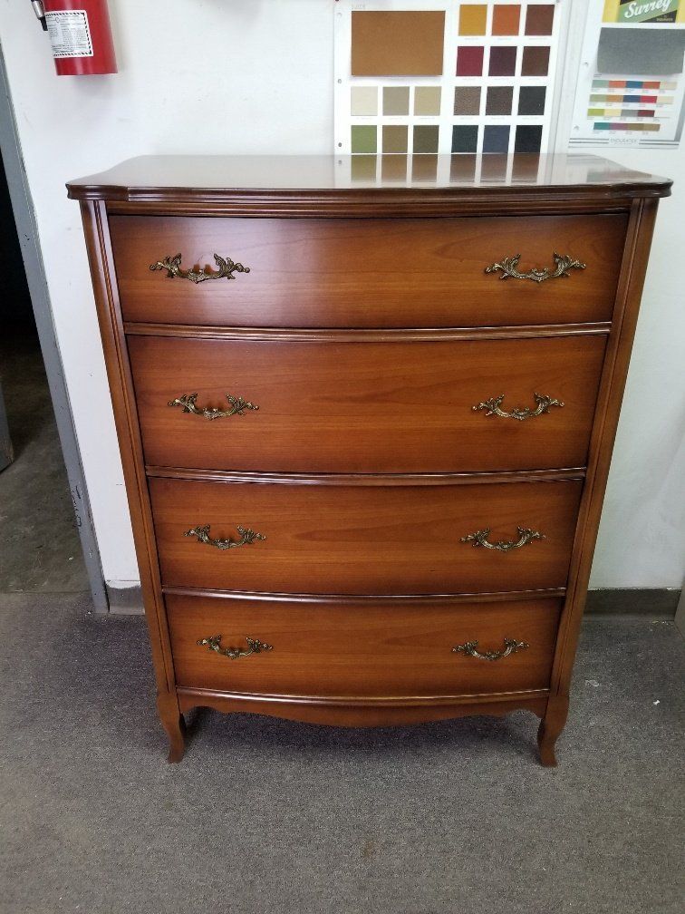 Vintage wooden dresser with four drawers and brass handles, standing against a wall in a room.