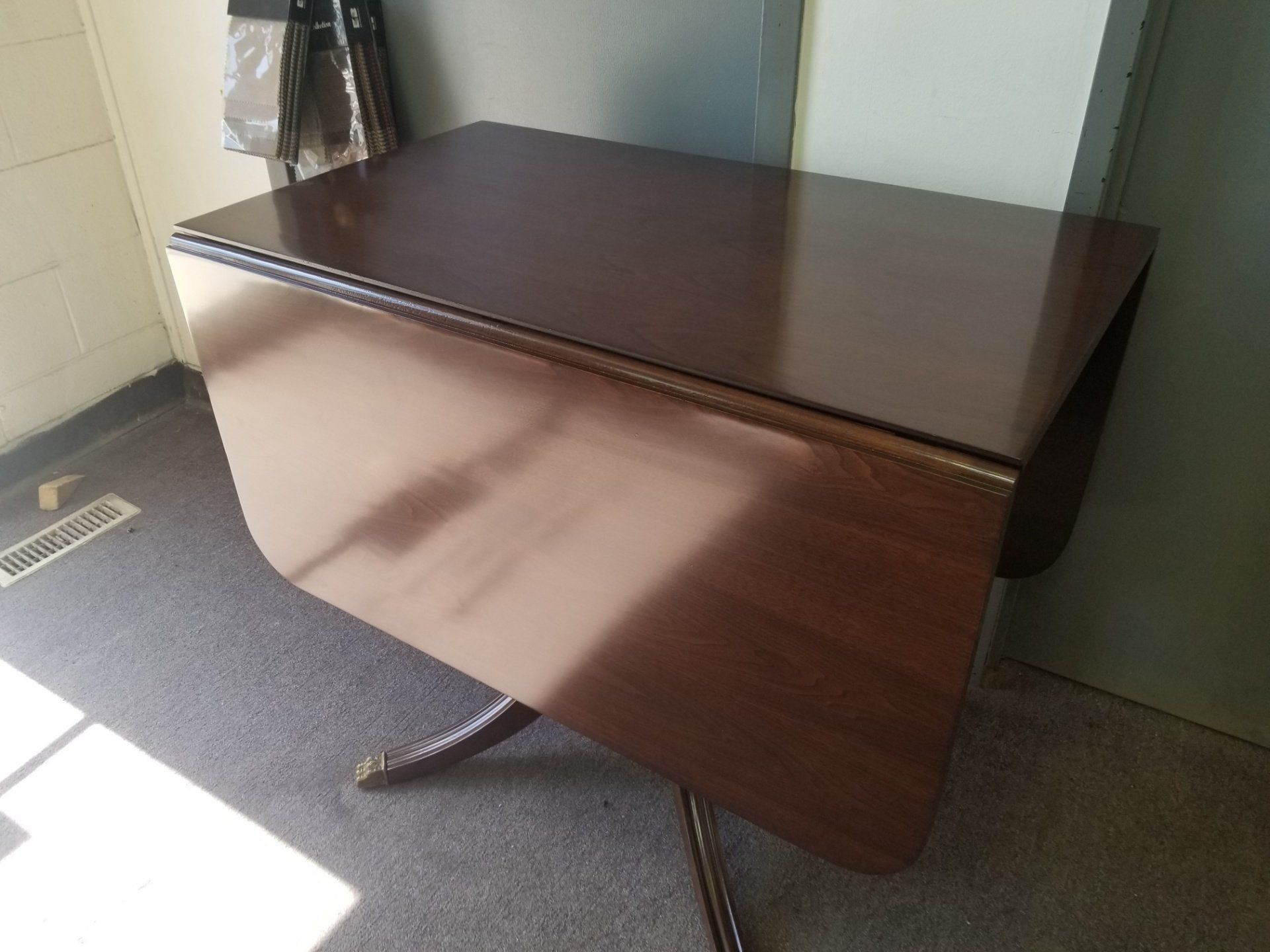 Dark wood drop-leaf table with one side folded down in a room by a wall and carpeted floor