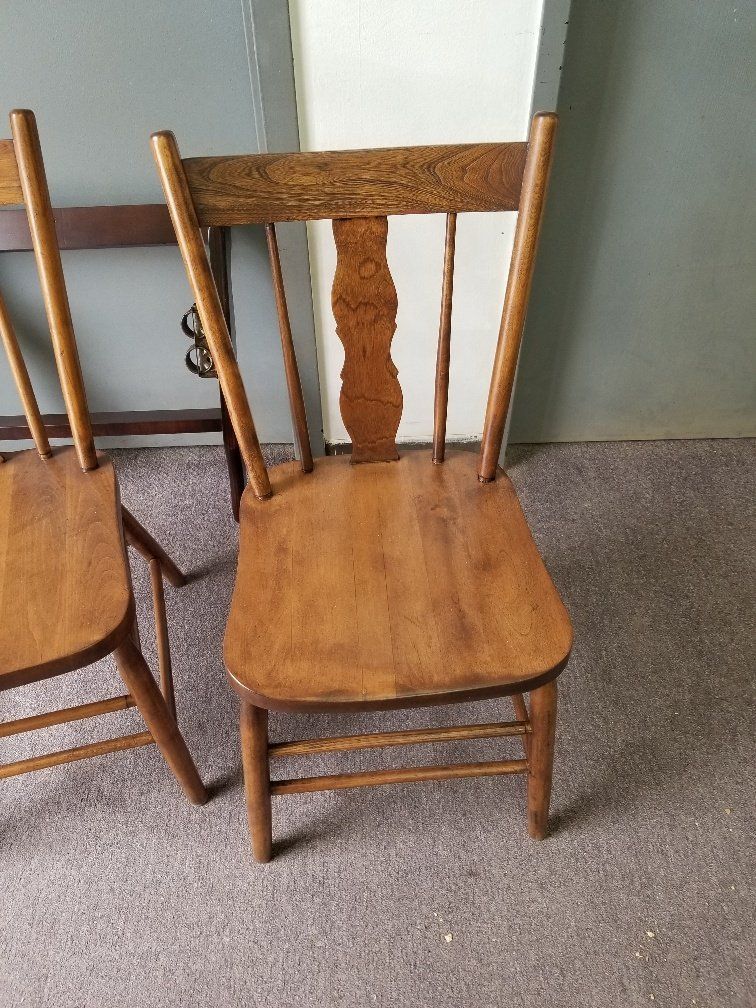 Wooden dining chair with woven seat on beige carpet beside another chair and a wall.