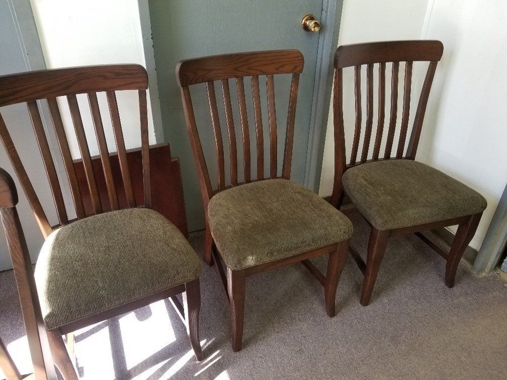 Three wooden dining chairs with green cushions lined up against a door and wall.