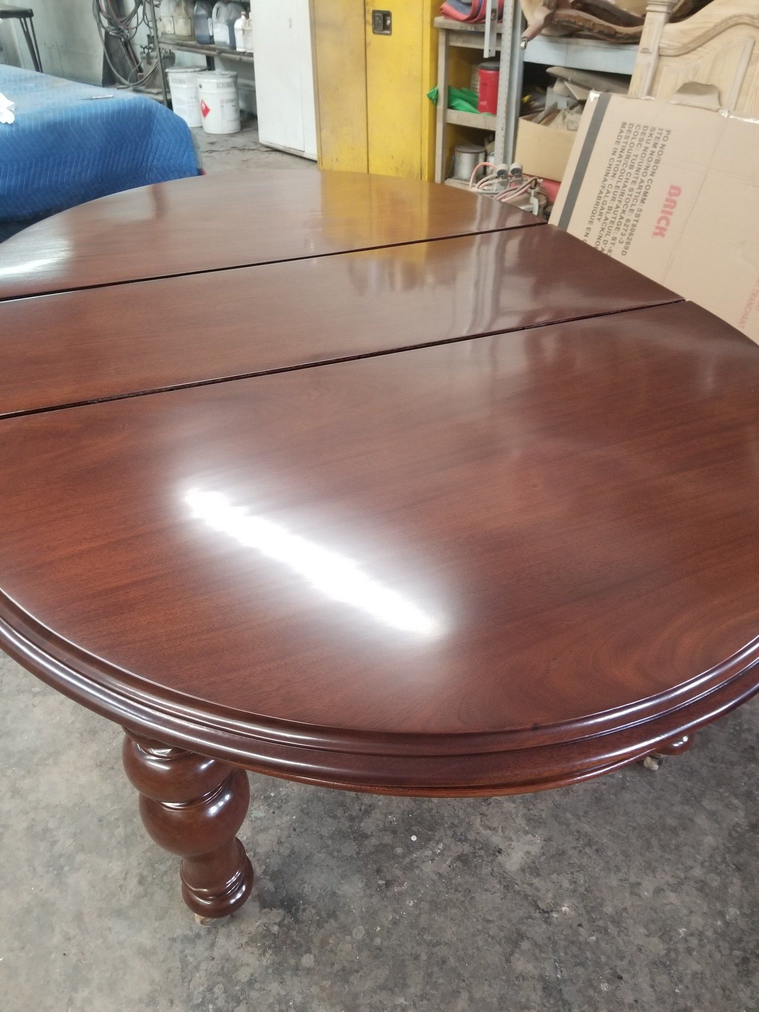 Dark wood oval dining table with one leaf in a storage room, with a blue chair nearby.
