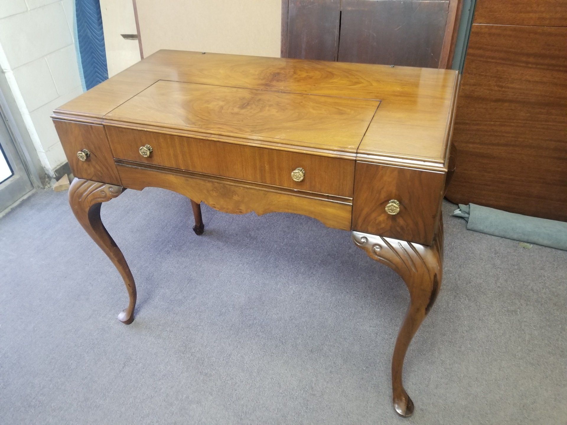 Antique wooden drop-leaf table with curved legs and drawers on a carpeted floor.