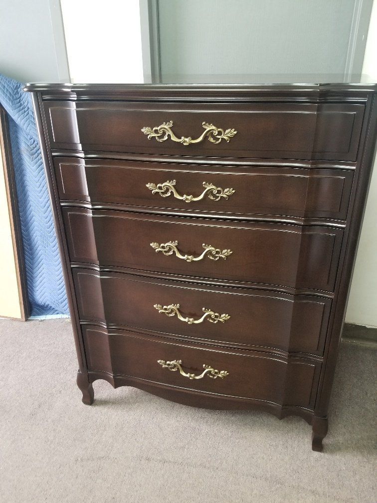 Dark wood five-drawer dresser with gold handles against a light wall and carpet.