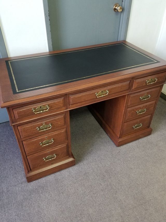 Wooden executive desk with black leather top, drawers on both sides, in an office