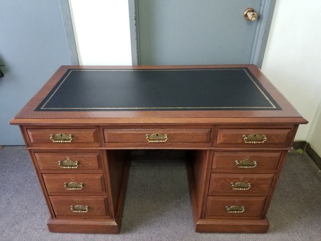 Wooden executive desk with black top and multiple drawers, centered in a room.