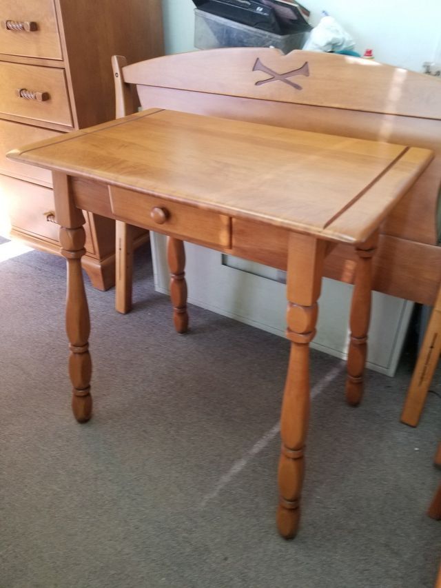 Wooden table with turned legs and a matching chair in a room with carpet and drawers