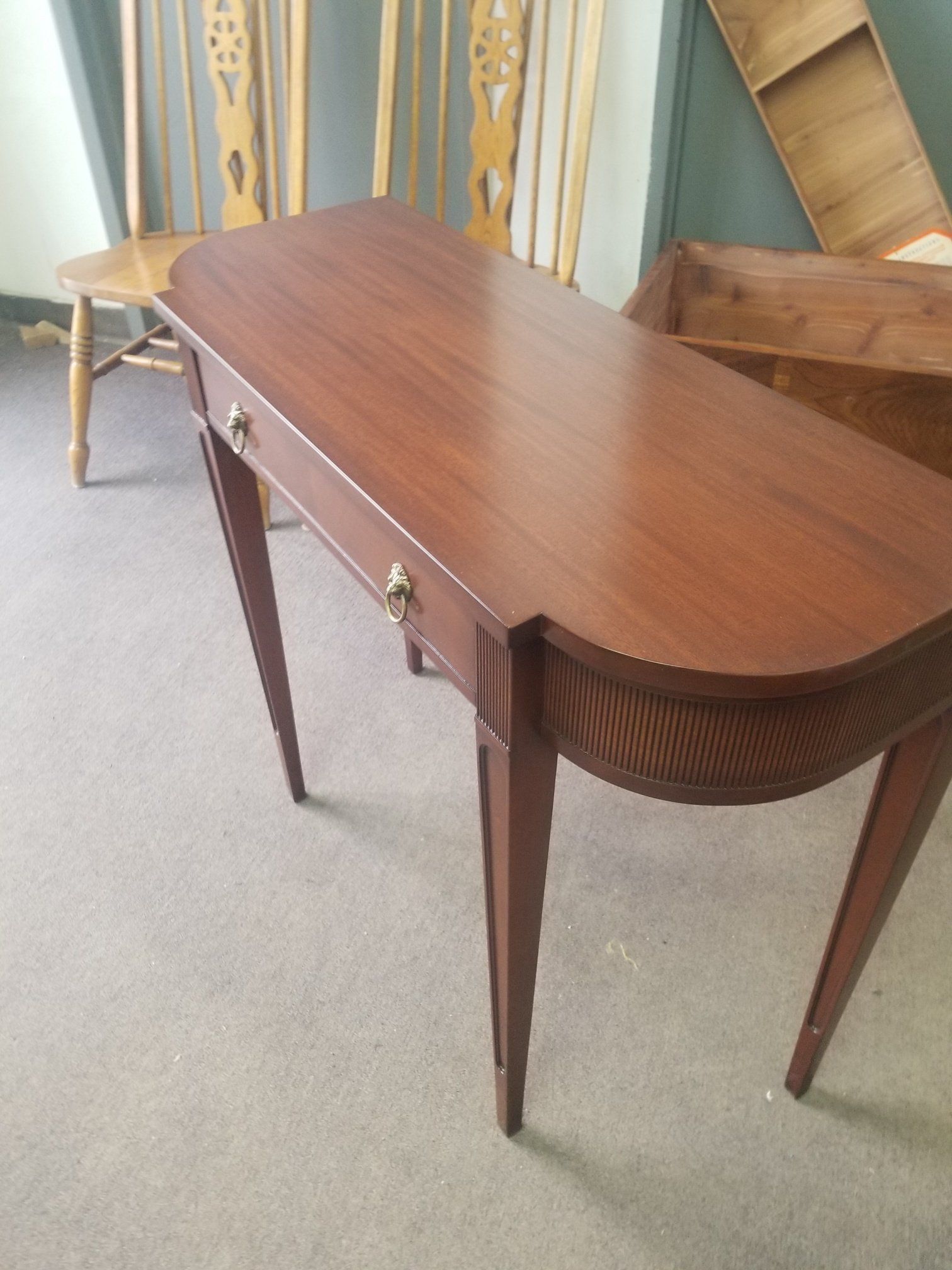 Brown wooden console table with tapered legs and a drawer, sitting indoors on a carpeted floor