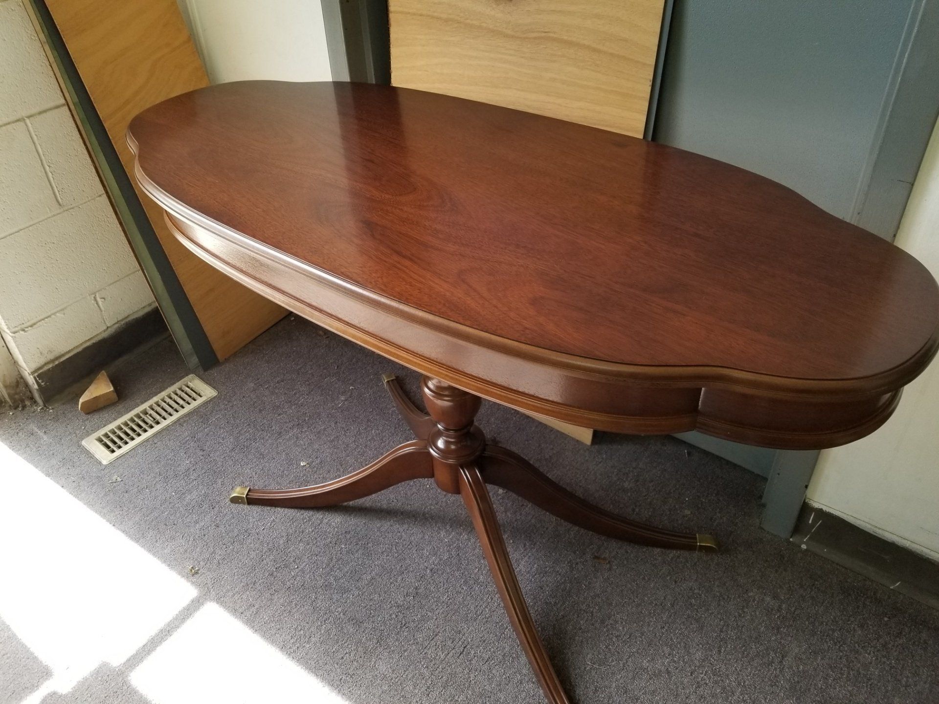 Oval wooden dining table with pedestal base in a room, near a door and vent