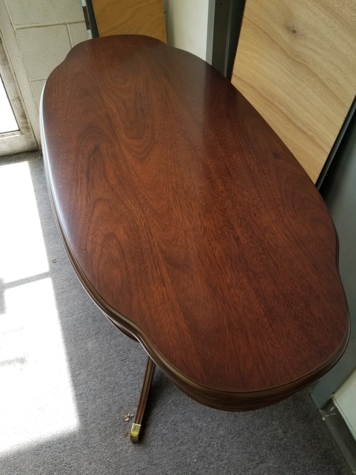Oval wooden table with one folded leg, leaning against a wall in a room.