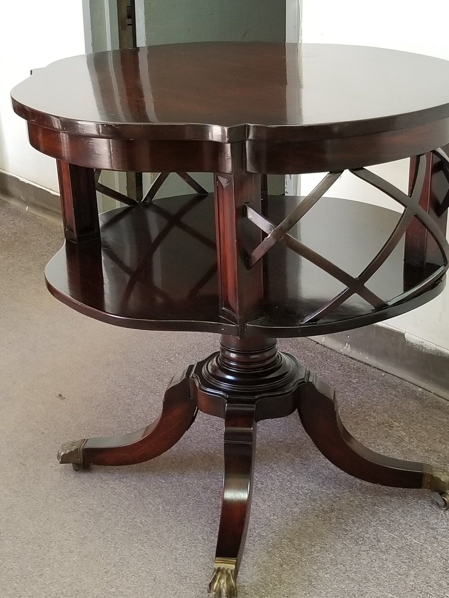 Dark wooden round pedestal table with curved legs and lattice sides on a carpeted floor