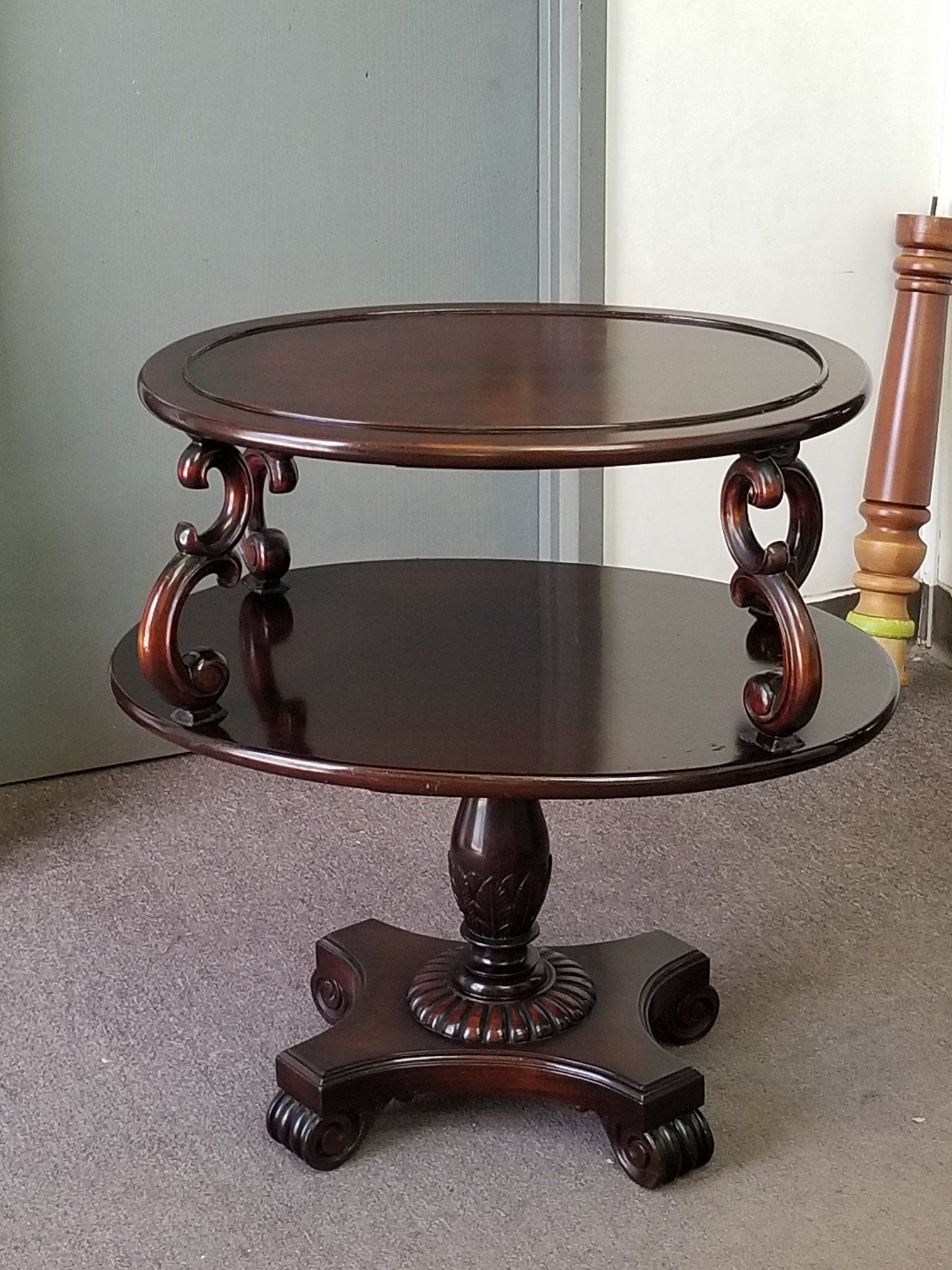 Dark wooden two-tier side table with a round top and lower shelf on a carpeted floor