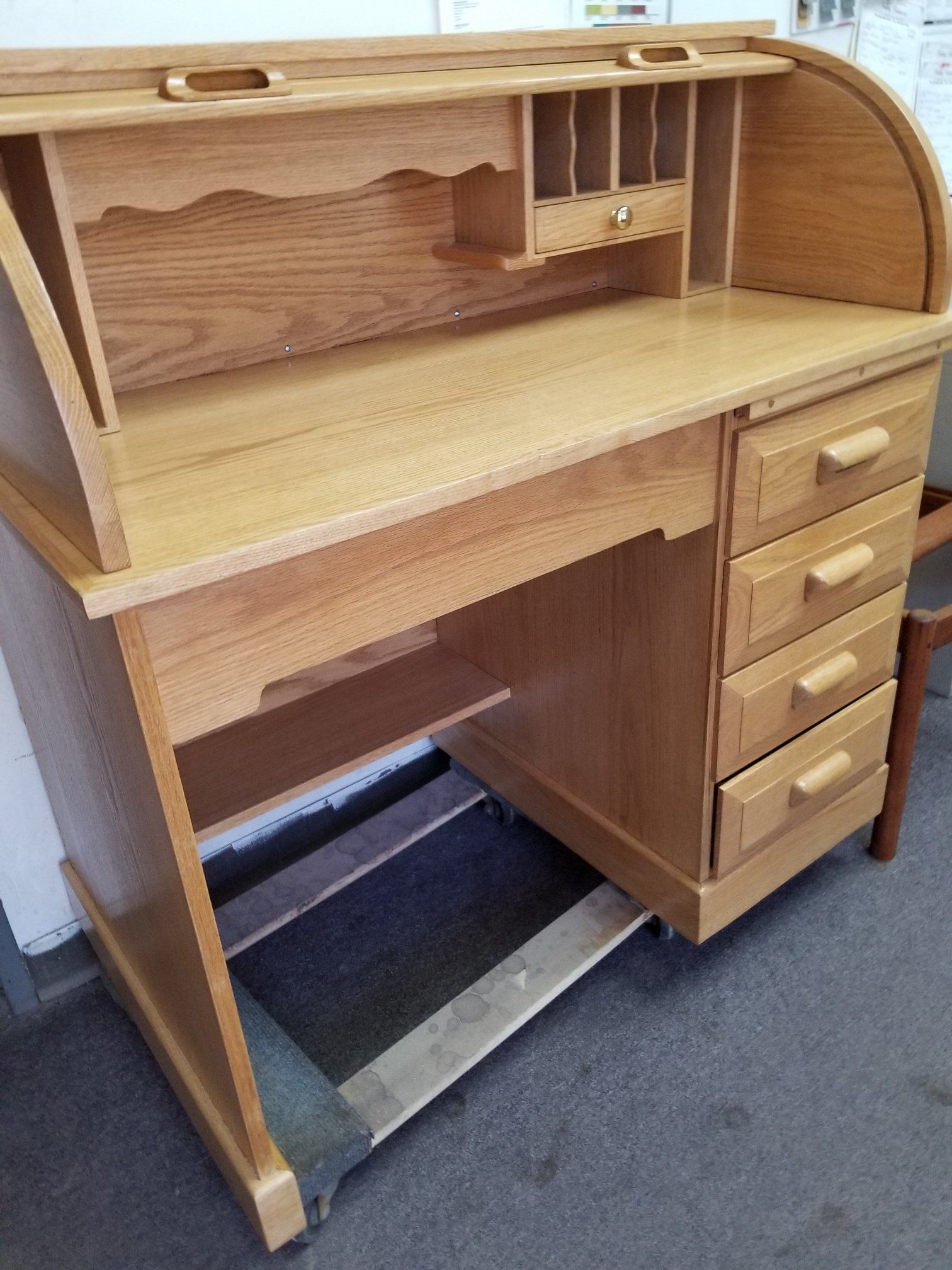 Wooden roll-top desk with drawers and open knee space on a carpeted floor