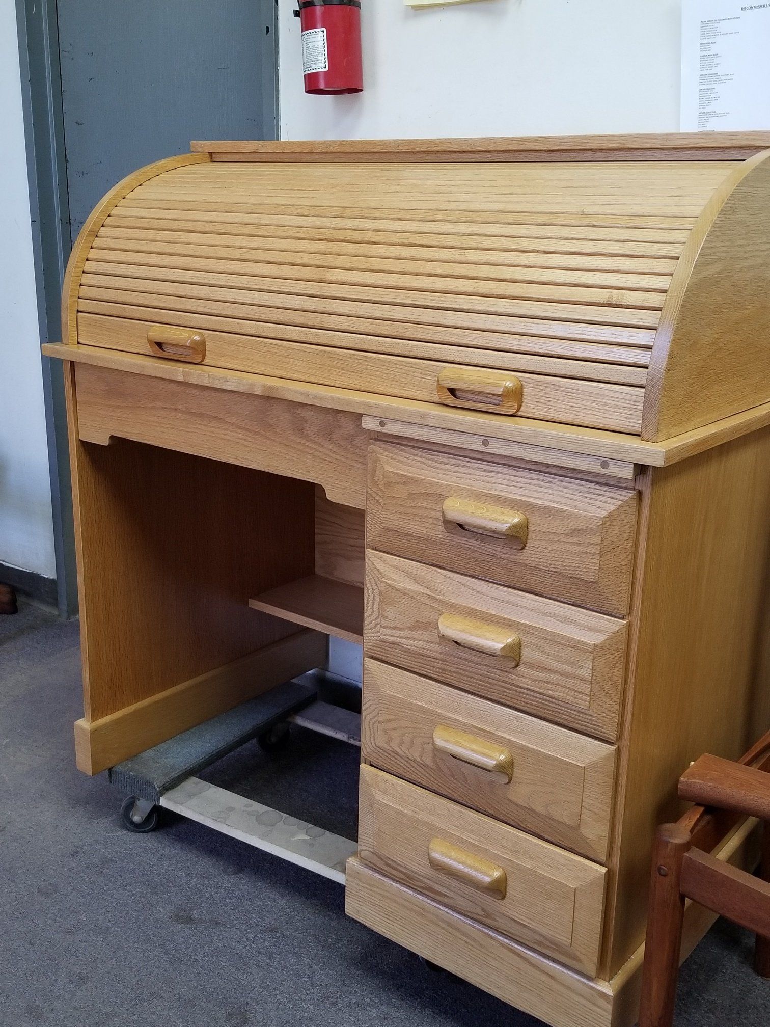 Wooden roll-top desk with four drawers in an office setting.