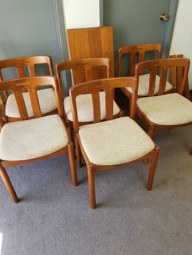 Five wooden chairs with beige cushions arranged in a room with carpet and a closed door