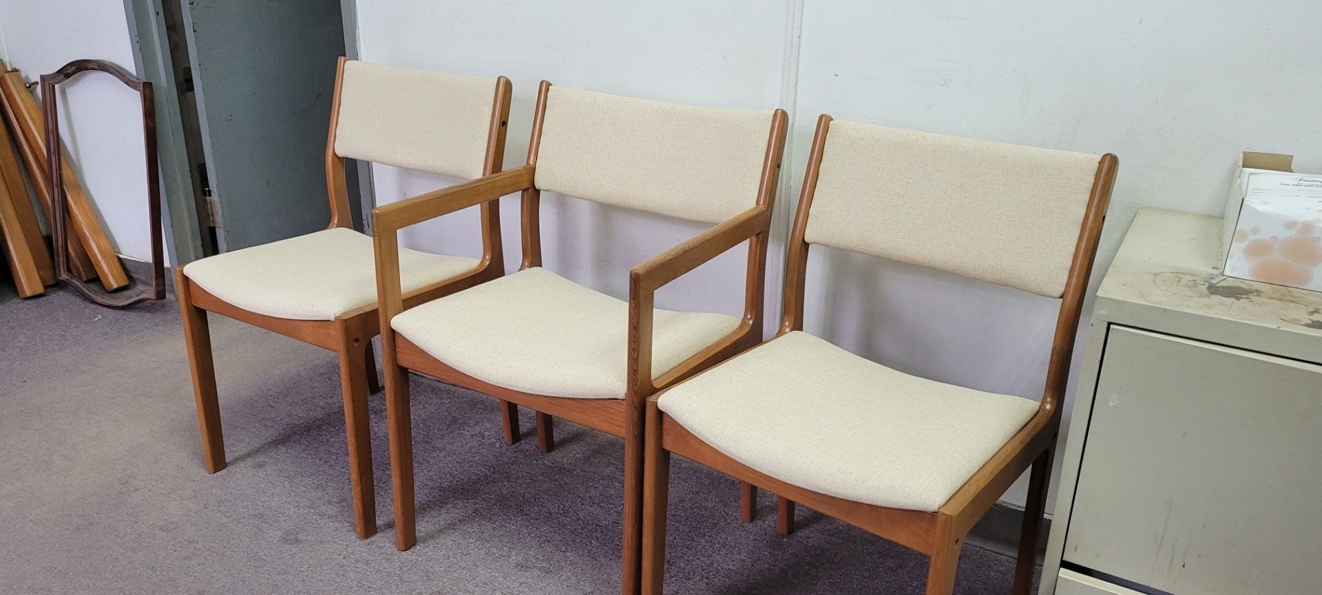 Three wooden chairs with beige seats lined up in an office waiting area