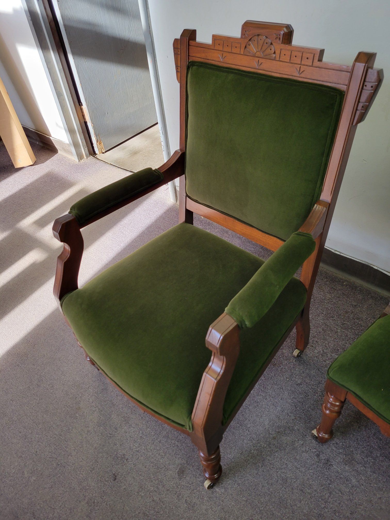 Green upholstered wooden armchair with carved details, shown indoors on a carpeted floor.
