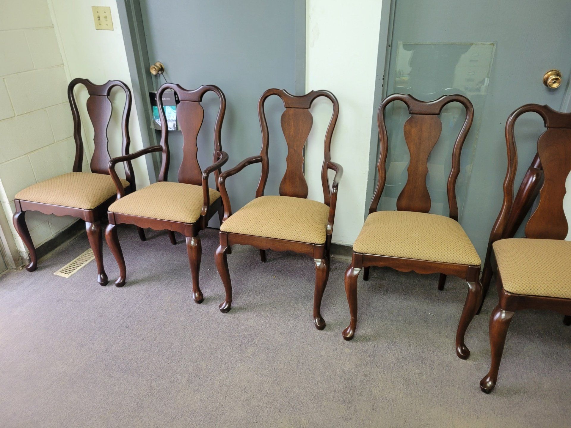Five upholstered wooden chairs lined against a wall in a carpeted room.