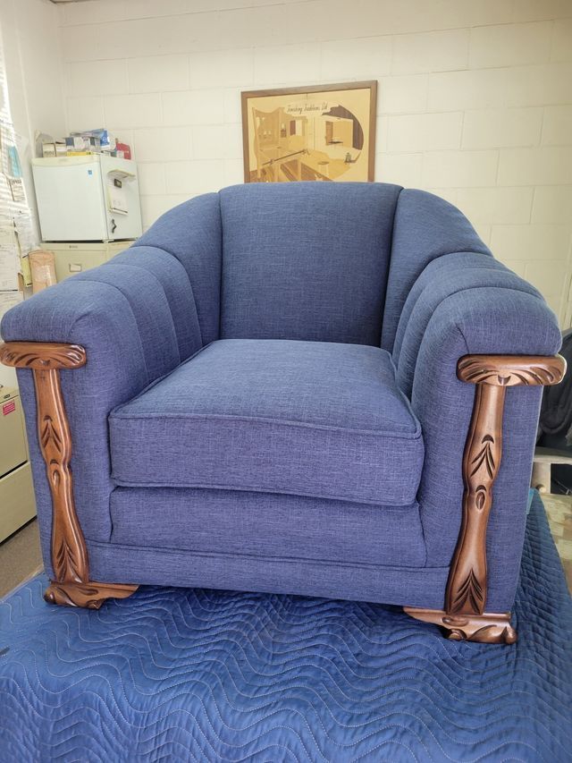 Blue upholstered armchair with carved wooden arms on a blue mat in a workshop or storage room