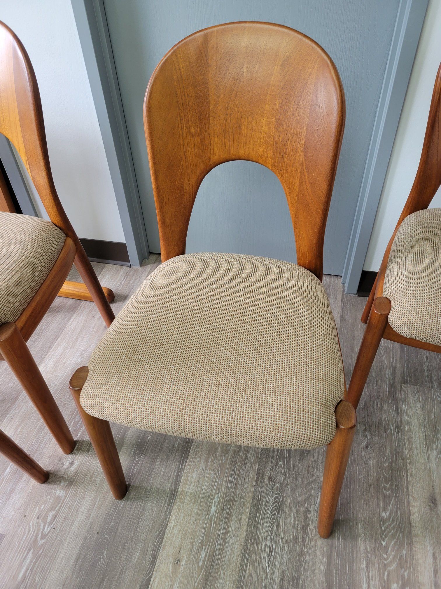 Wooden chair with beige woven seat cushion between two chairs on a gray floor