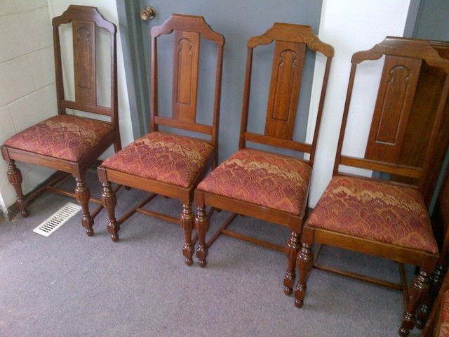 Four wooden dining chairs with red patterned seats lined up on a carpeted floor