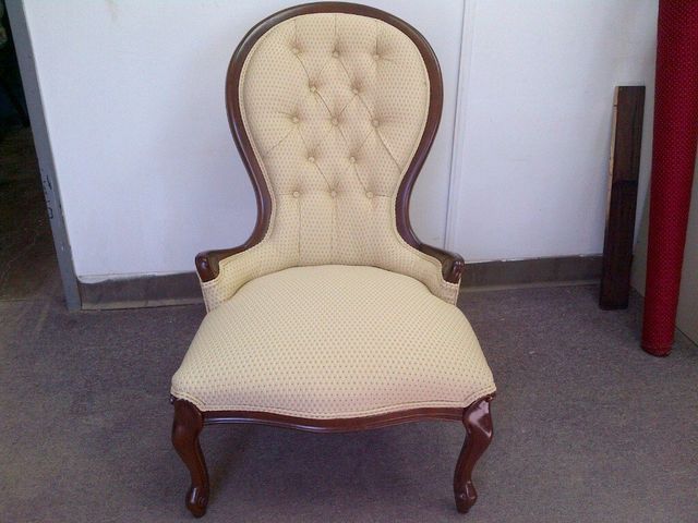 Cream tufted upholstered armchair with wooden legs against a white wall and gray carpet.