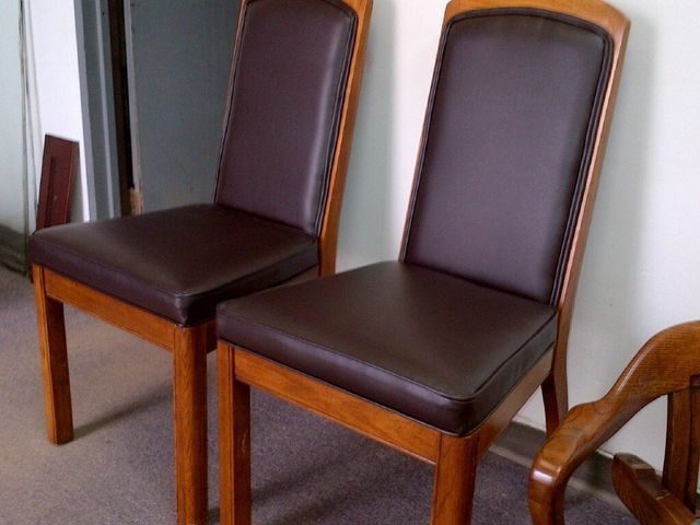 Two dark brown upholstered chairs with wooden legs against a light wall