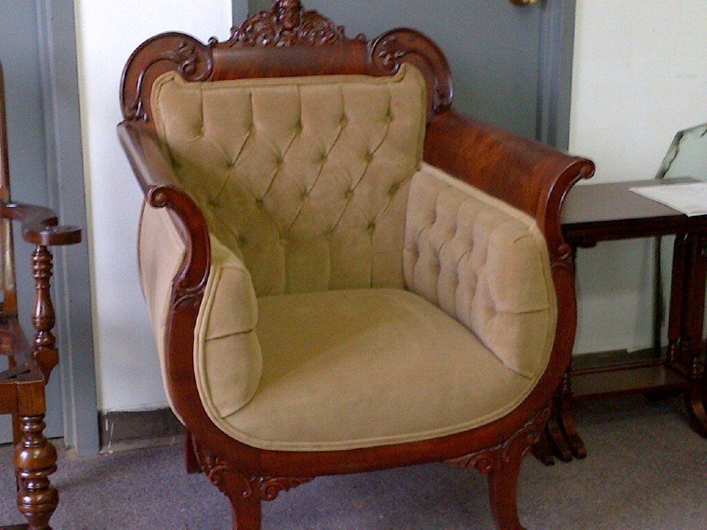 Antique upholstered armchair with carved wooden frame and tan tufted back in a room