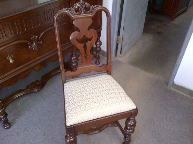 Ornate wooden chair with a cream cushion beside a carved wooden sideboard in a hallway