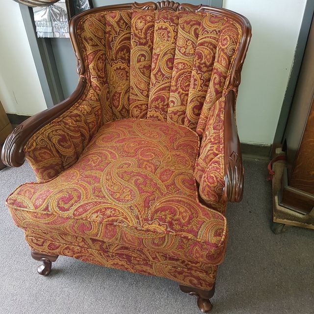 Vintage red and gold patterned upholstered armchair with wooden arms in a room