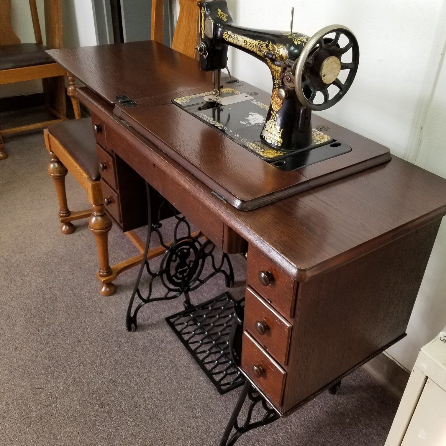 Antique black sewing machine on a dark wooden sewing table in a carpeted room.