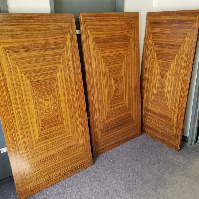 Three wooden cabinet doors with geometric veneer patterns leaning against a wall on a carpeted floor