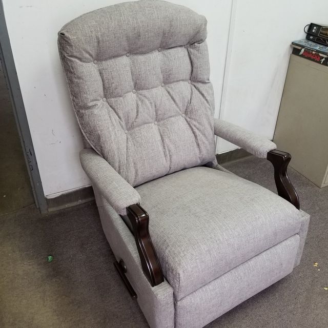 Light gray upholstered recliner chair with dark wooden arms against a wall on a carpeted floor