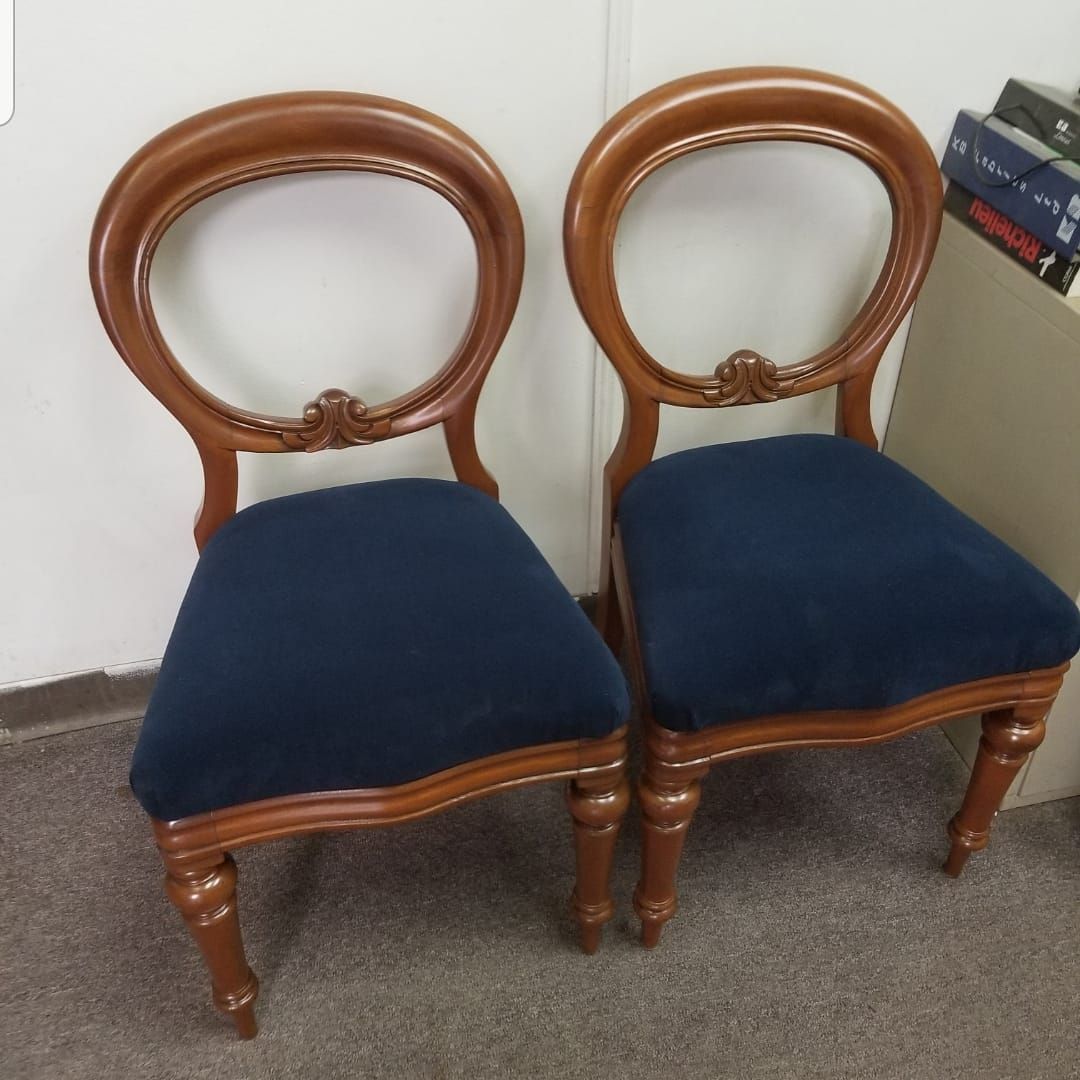 Two wooden chairs with blue upholstered seats against a white wall.