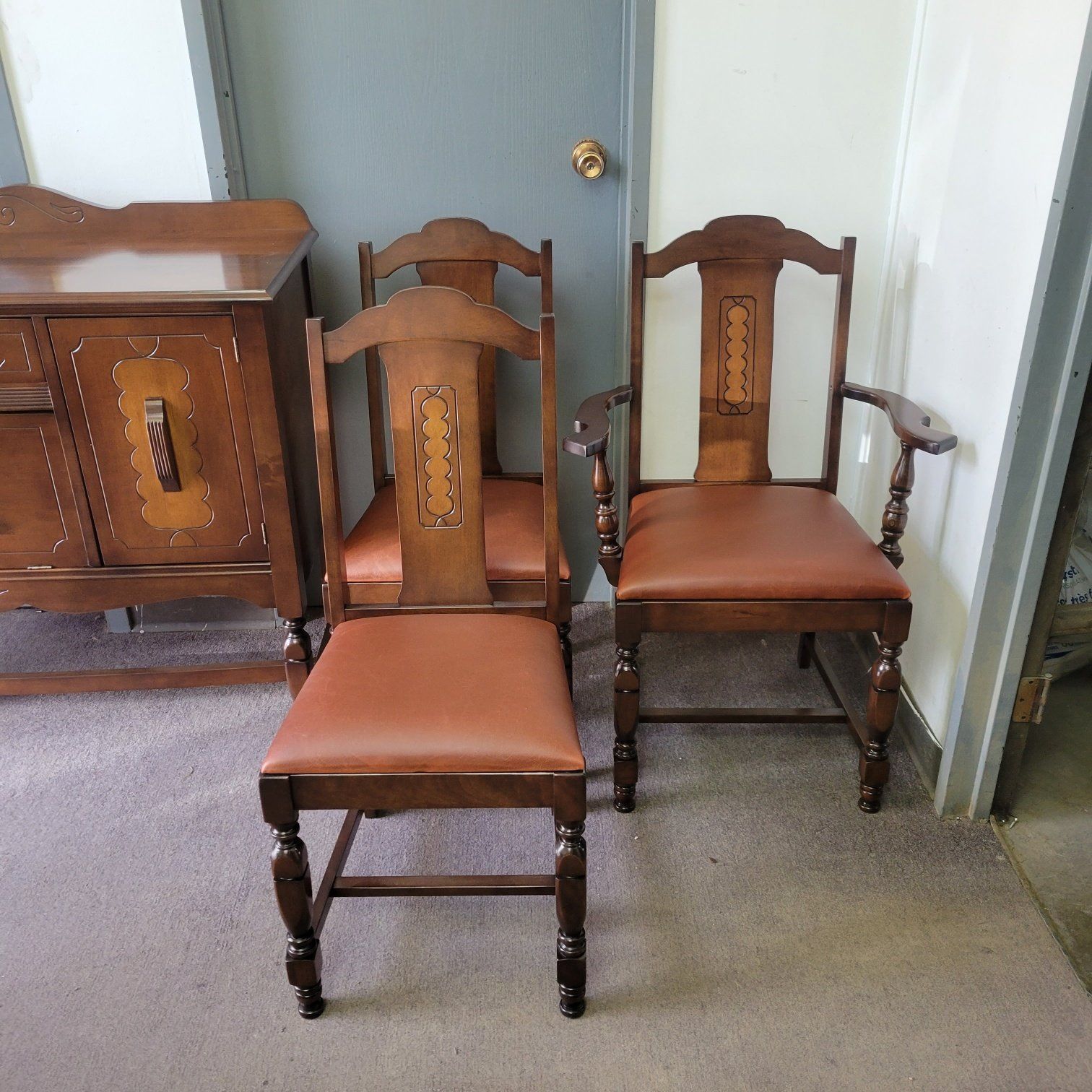 Two wooden dining chairs with brown cushions in a carpeted room near a cabinet