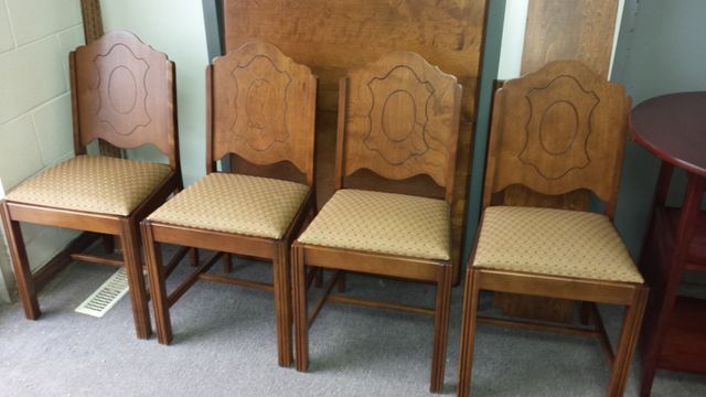 Four wooden dining chairs with woven seats lined up against a wall, with a small red side table at right.