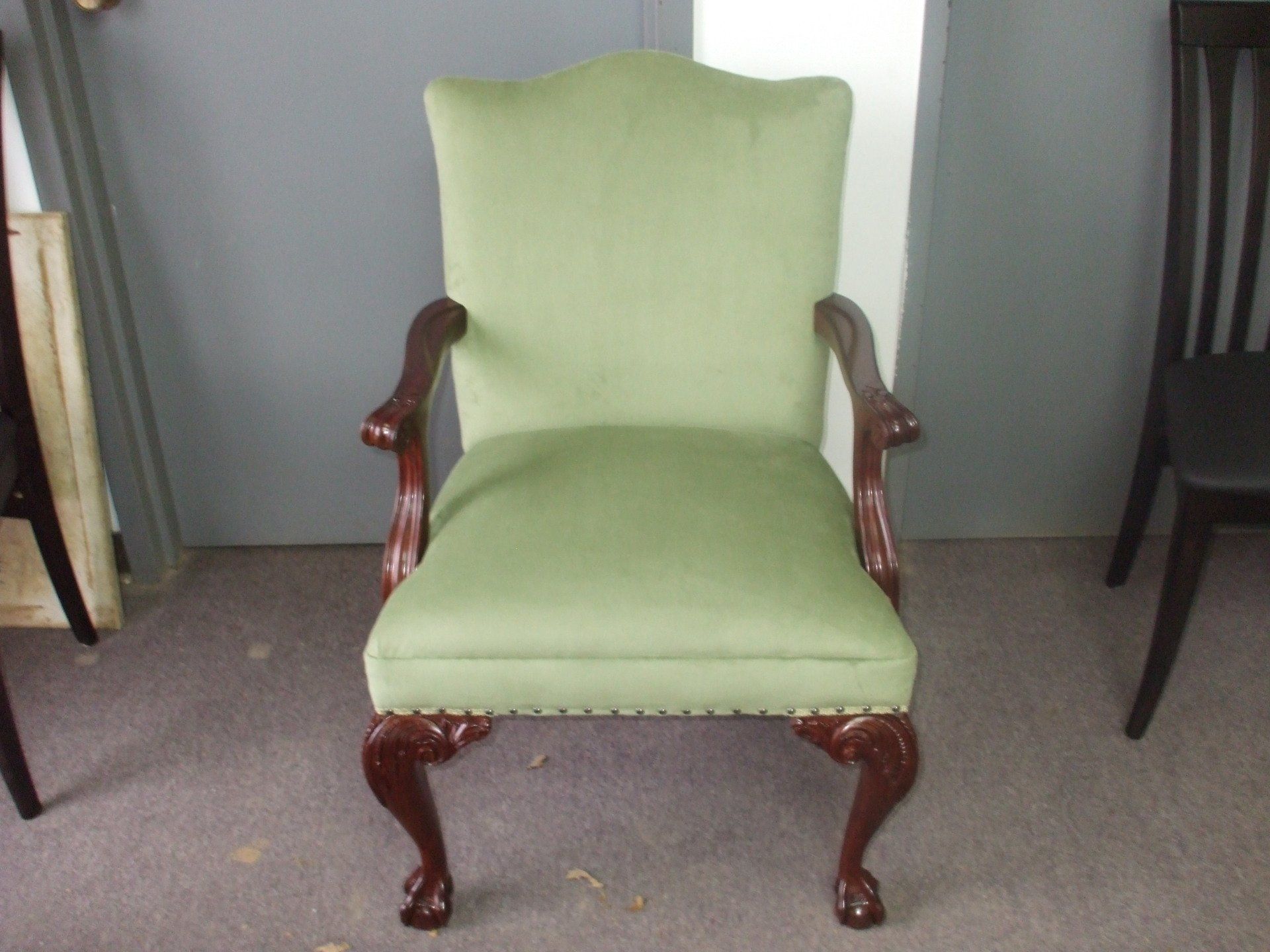 Light green upholstered armchair with carved wooden arms and legs on a carpeted floor