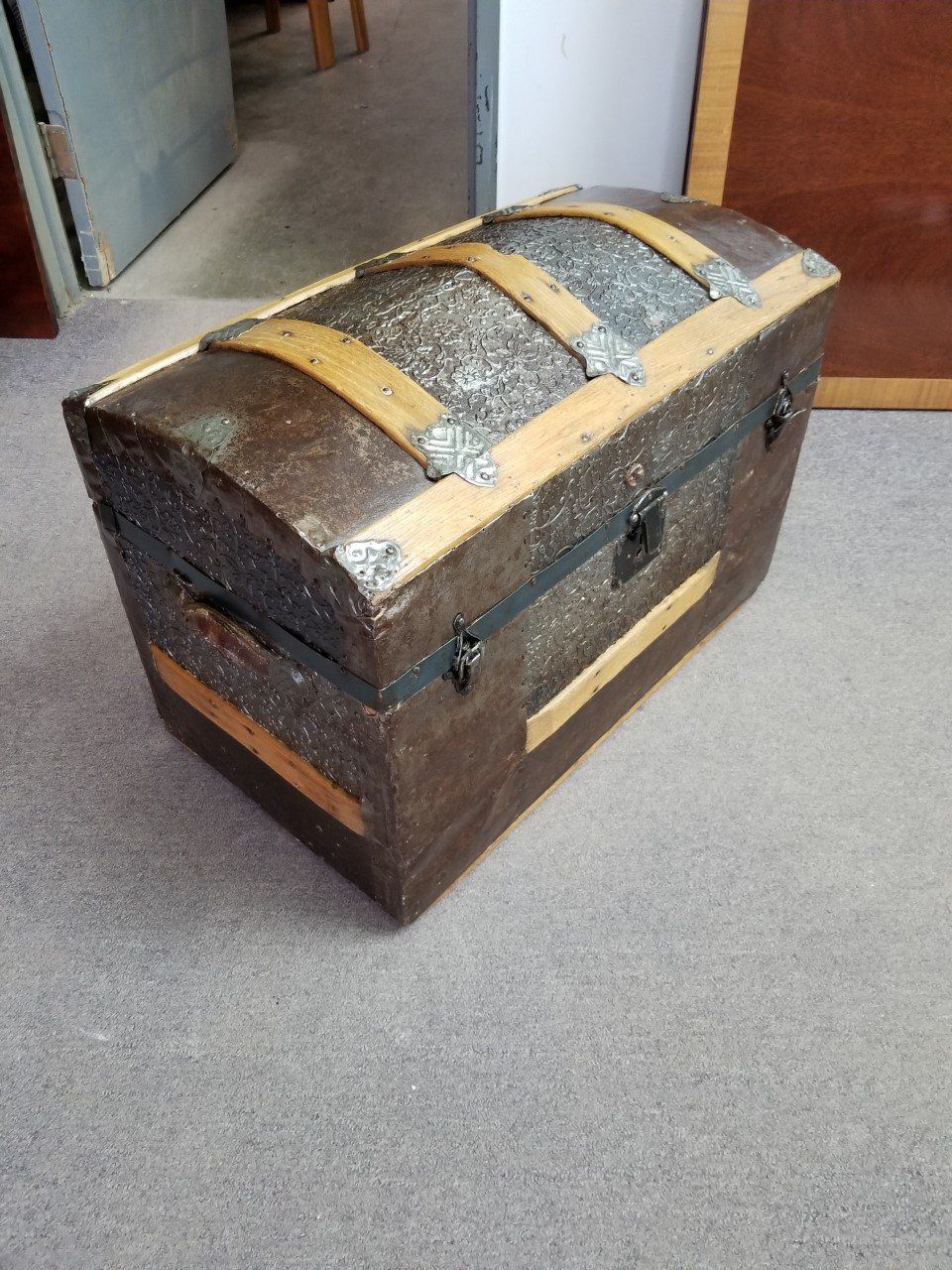 Old wooden treasure chest with metal bands, sitting on a carpeted floor.
