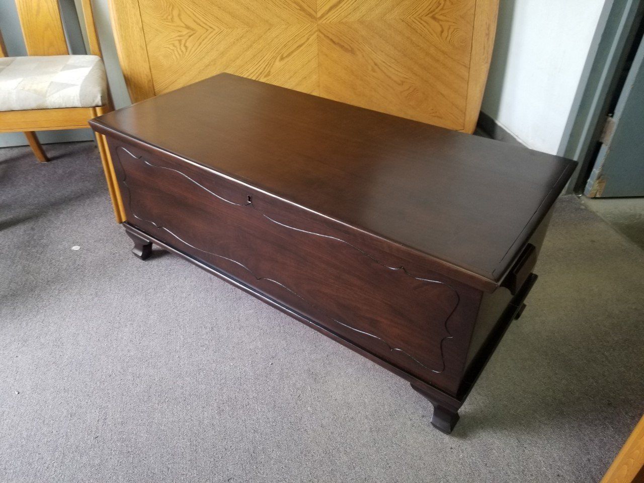 Dark wooden storage chest with lid and legs on a carpeted floor