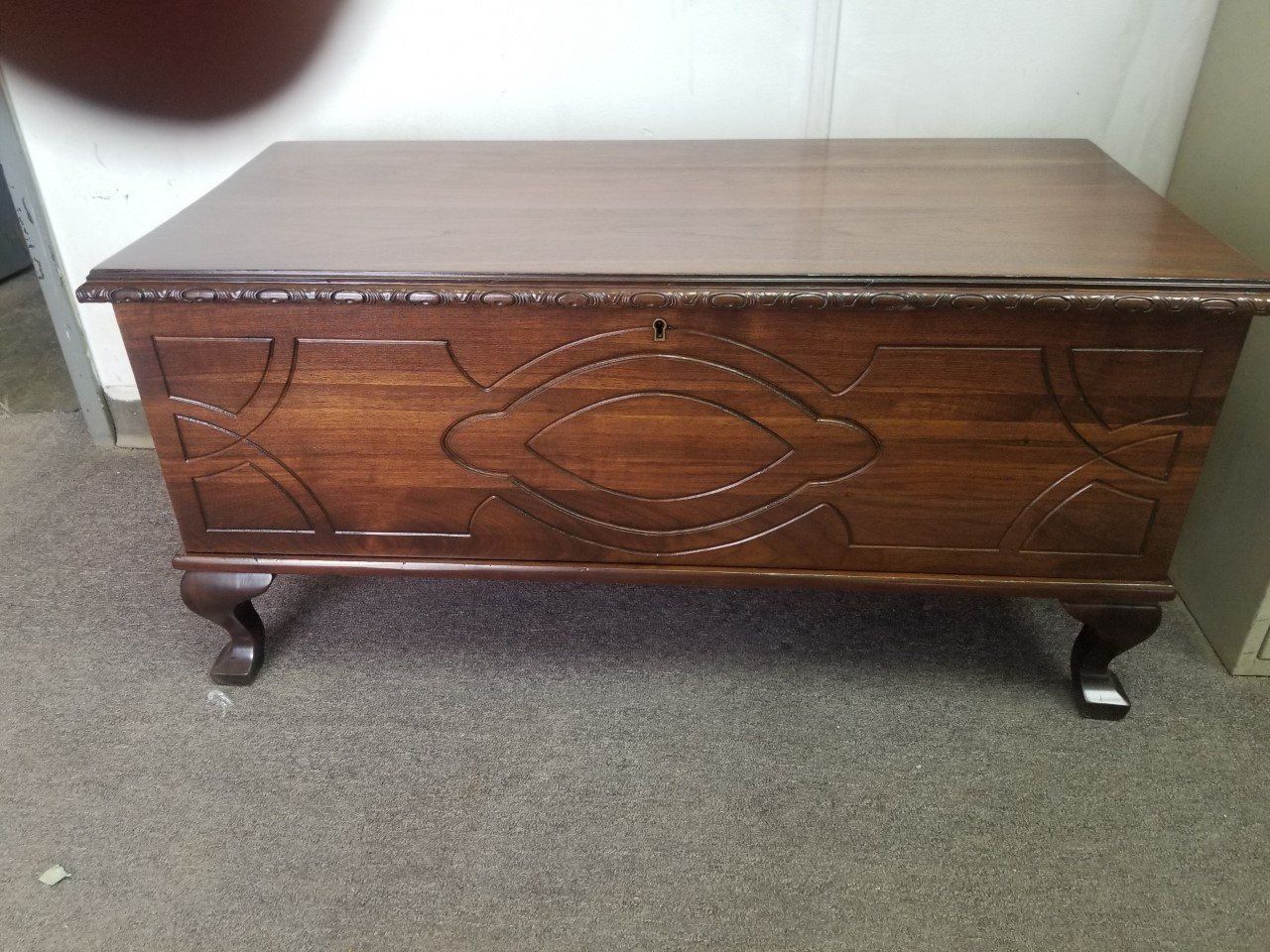 Dark wooden storage chest with carved front panel and small legs on carpeted floor