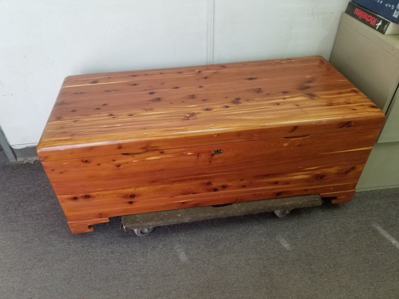 Wooden storage chest with a hinged lid on a carpeted floor against a white wall.