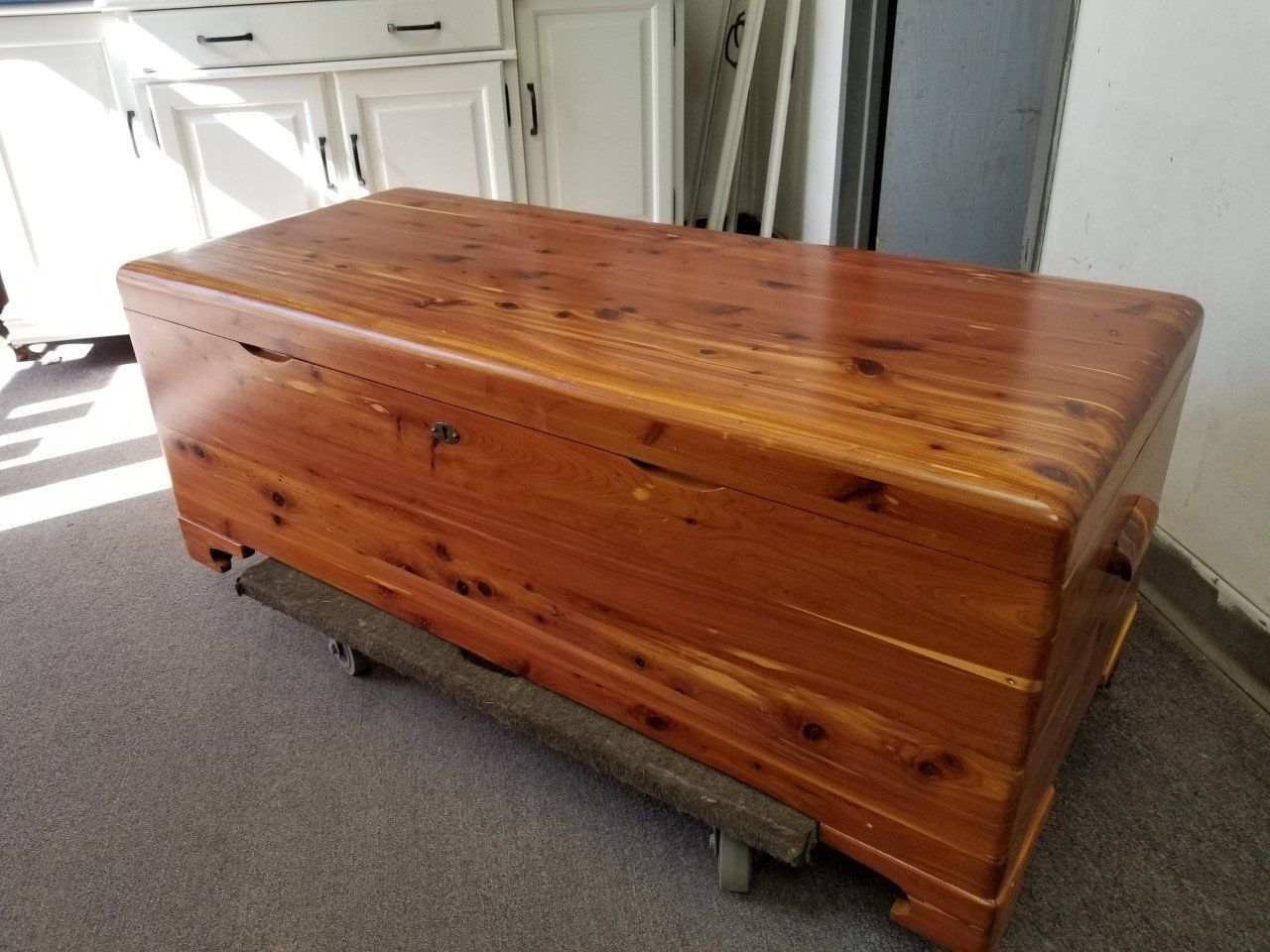 Large polished wooden chest on a dolly in a room with white doors and gray carpet.