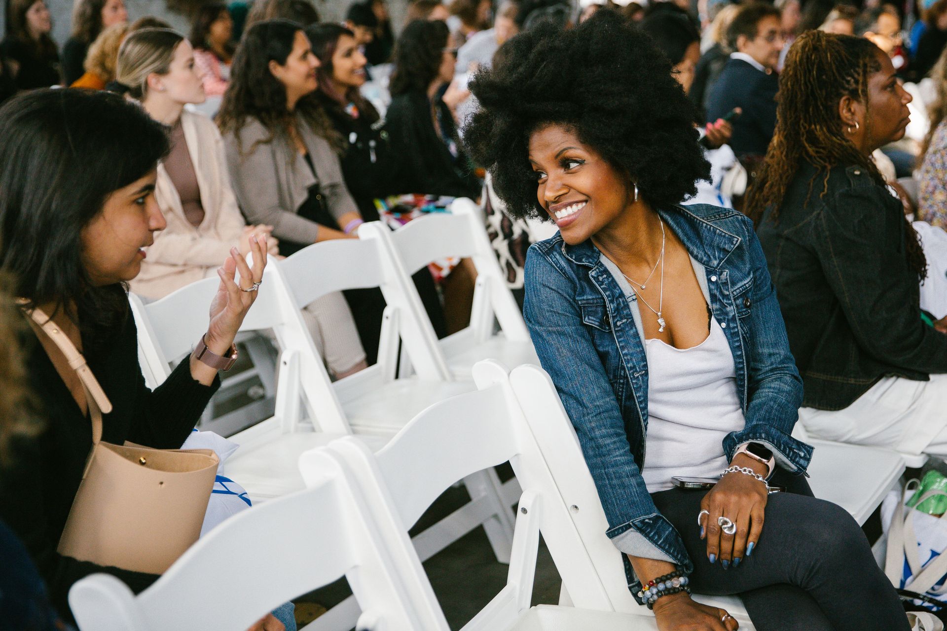 A group of women are sitting in white folding chairs at a conference.