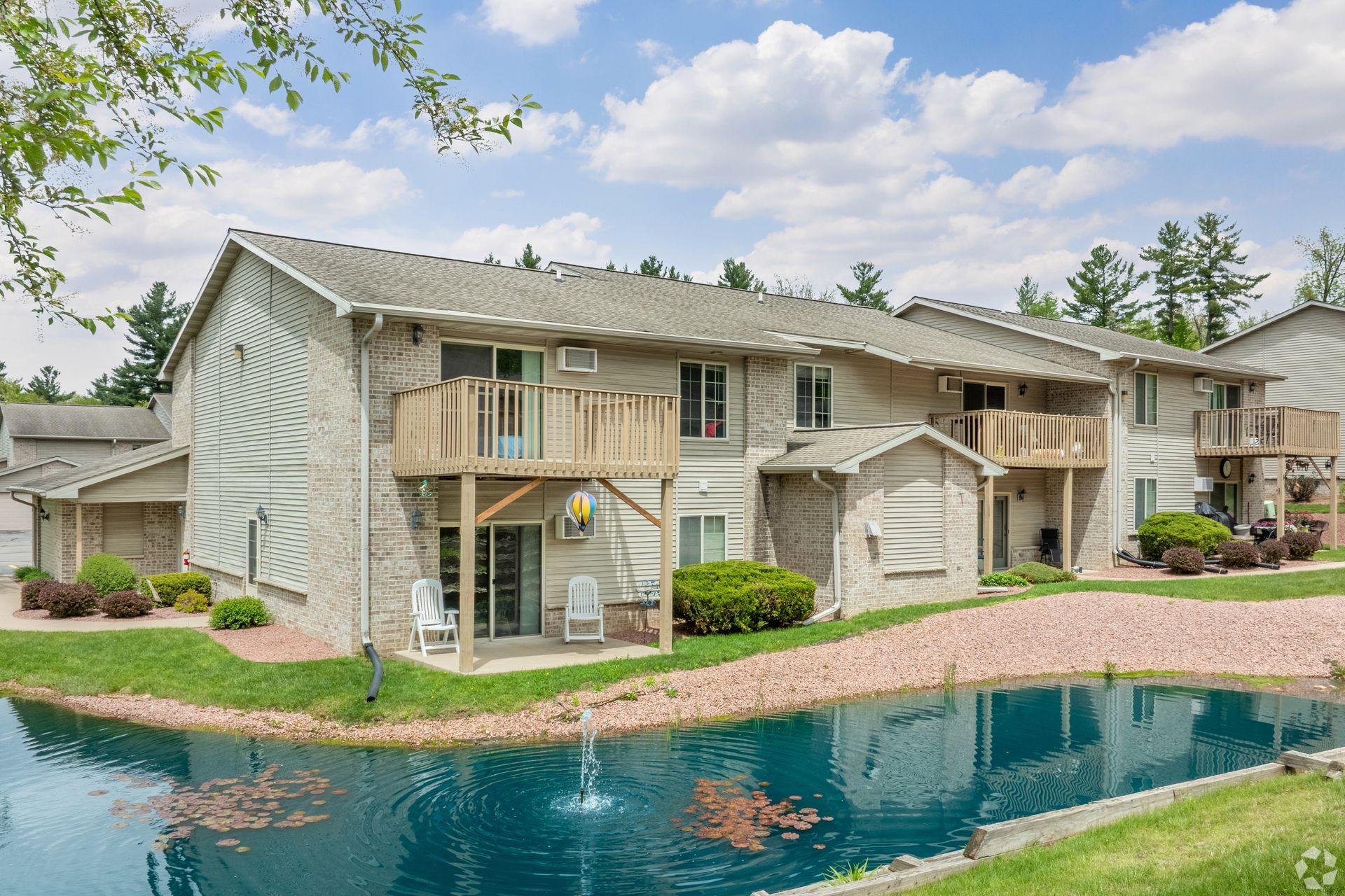 Apartment complex with balconies beside a turquoise pool under a partly cloudy sky