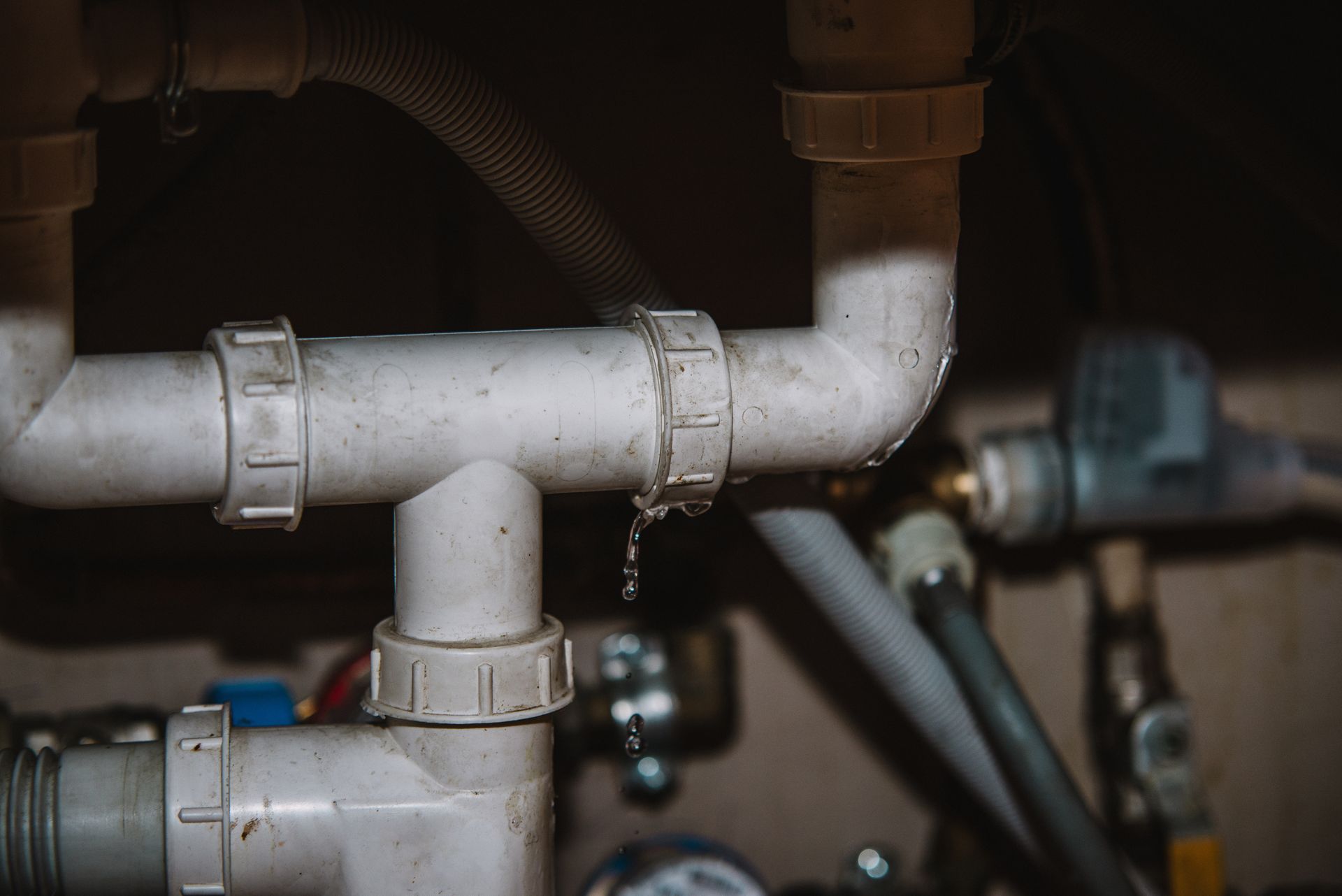 A leaking PVC pipe under a sink showing water droplets, highlighting the need for plumbing leak repair